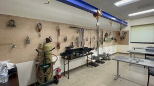 Photograph of a classroom at the Ironworkers Local 5 apprenticeship training facility. Various types of rigging equipment hanging on a wall.